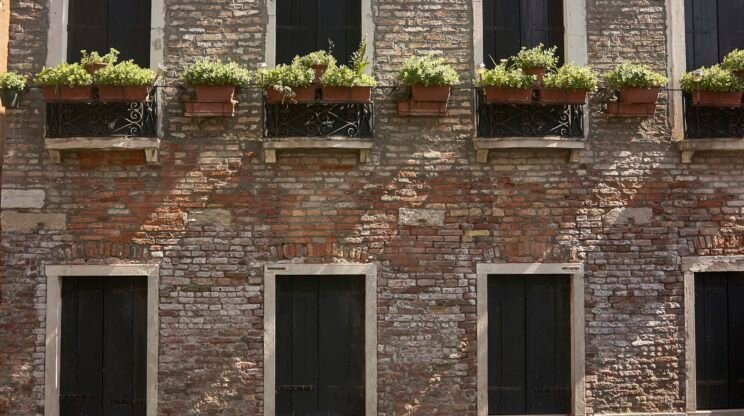 Facade of an ancient palace with exposed bricks and numerous windows arranged on two floors.